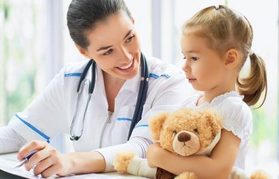 Eine Kinderärztin spricht mit einem jungen Mädchen, das einen Teddybären festhält.