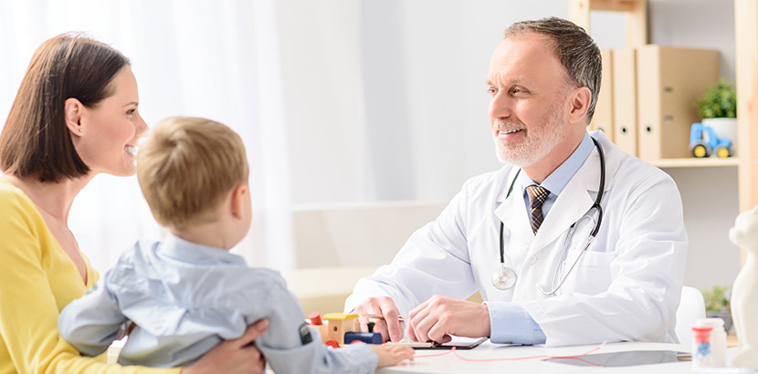 Eine Mutter und ihr Sohn sitzen mit einem Kinderarzt am Schreibtisch.