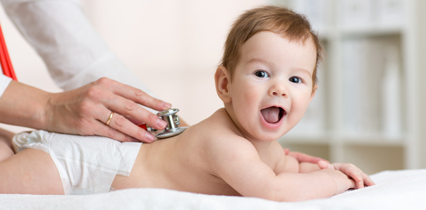 Eine Kinderärztin verwendet ein Stethoskop um die Daten des Herzschlags eines fröhlichen Babys zu messen.