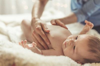 Baby mit Neurodermitis, das auf einer Lammfelldecke liegt und von der Mutter gestreichelt wird.