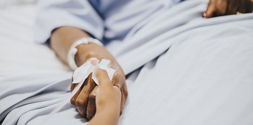 Eine Person in einem Krankenhausbett, die die Hand einer anderen Person hält.