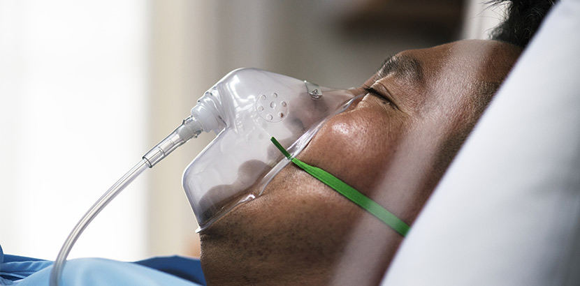 Ein Mann mit geschlossenen Augen und Sauerstoffmaske, der in einem Krankenhausbett liegt.