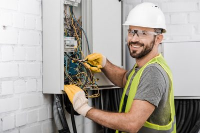 Hübscher lachender Elektriker, der an einer Kabelbox arbeitet. Elektriker Wien.