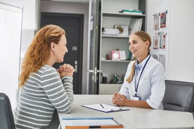 Rothaarige Frau bei der Beratung bei ihrer Gynäkologin, am Tisch sitzend. Frauenarzt Graz.