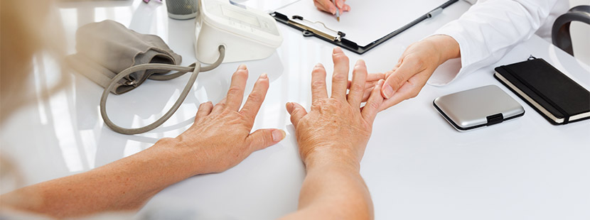 Ärztin, die die Hände einer Patientin untersucht, die von Rheuma geschwollen sind. Rheumatologe Wien.