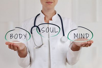Ärztin, die drei Sprechblasen in den Händen hält, in denen Mind, Body, Soul geschrieben steht. Steht für ganzheitliche Zahnmedizin Wien.