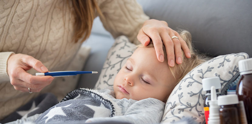 Eine Mutter, die ihrem kranken Kind die Hand auf die Stirn legt und einen Fieberthermometer hält. Kawasaki Syndrom