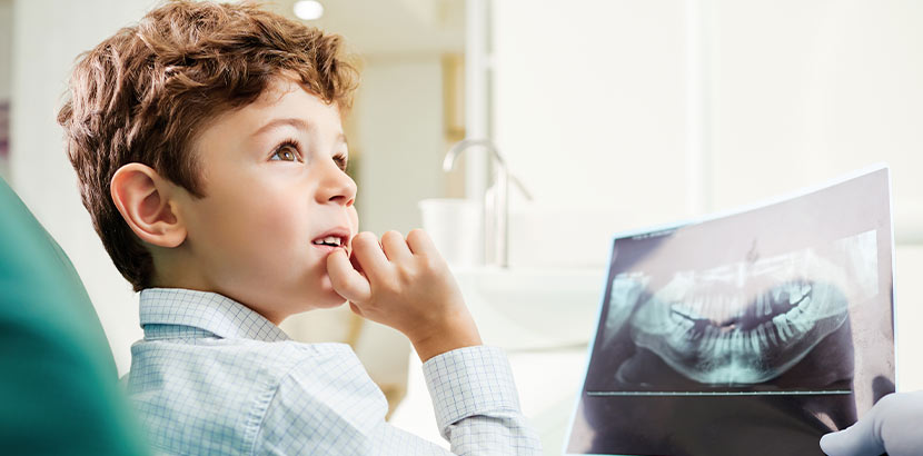 Kleiner Junge im Behandlungsstuhl beim Kieferorthopäden, der ihm ein Röntgenbild seiner Kiefer zeigt. Kieferorthopäde Wien.