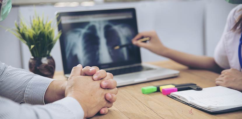 Lungenfachärztin im Gespräch mit einem Patienten. Am Laptop ist das Röntgenbild der Lungen zu sehen.