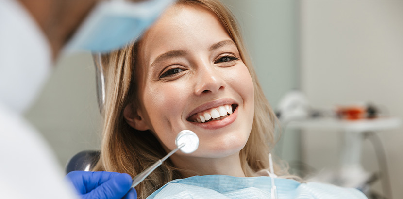 Eine blonde Frau, die im Zahnarztstuhl sitzt und lächelt.