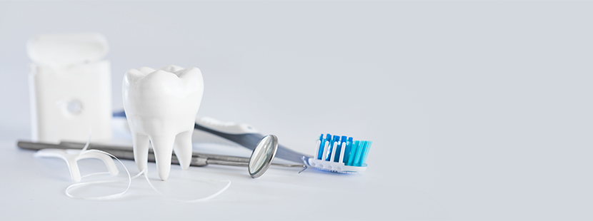 Eine Zahnbürste, eine Packung Zahnseide, ein Mundspiegel und ein Modellzahn, die vor einem grauen Hintergrund liegen.