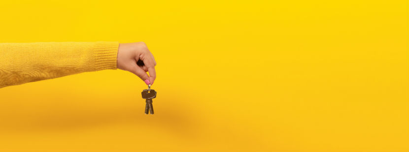 Wohnungssuche: weiblicher Unterarm hält einen Schlüssel in der Hand vor gelbem Hintergrund