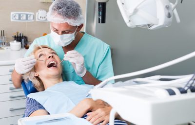 Ein Zahnmediziner untersucht eine Patientin, die auf dem Zahnarztstuhl sitzt.