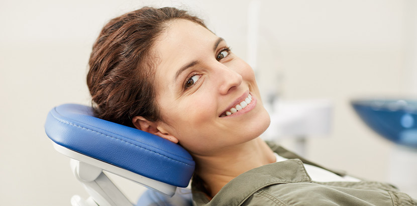 Eine lächelnde Frau liegt auf dem Behandlungsstuhl einer Zahnarztpraxis.