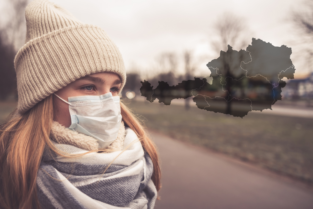 Junge Frau mit Atemschutzmaske, im Hintergrund eine Weltkarte mit Corona-Gebiet.