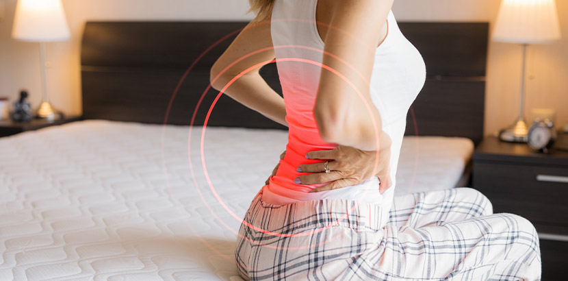 Eine Betroffene des Fibromyalgie Syndrom sitzt mit Rückenschmerzen im Bett.
