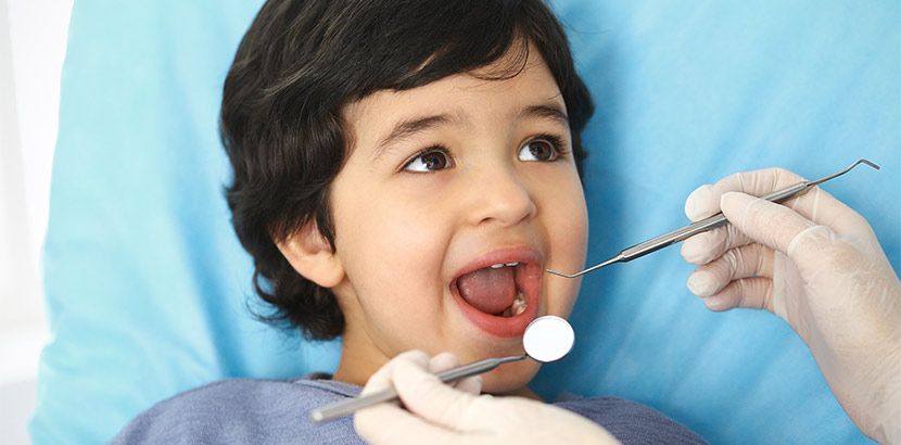 Ein Zahnarzt verwendet eine Zahnsonde und einen Mundspiegel um einen Jungen zu untersuchen.