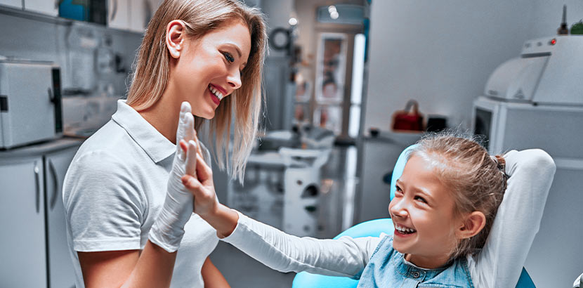 Ein junges Mädchen gibt ihrer Kinderzahnärztin ein High Five.