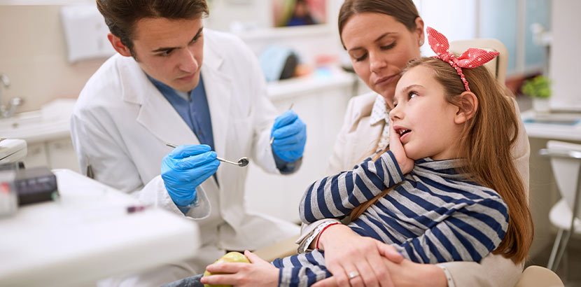 Eine Mutter urmarmt ihre Tochter schützend während der Zahnarzt sie behandeln möchte.