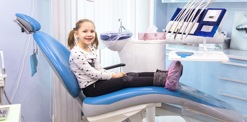 Ein Mädchen mit Zöpfen sitzt auf dem Behandlungsstuhl in einer Zahnarztpraxis.