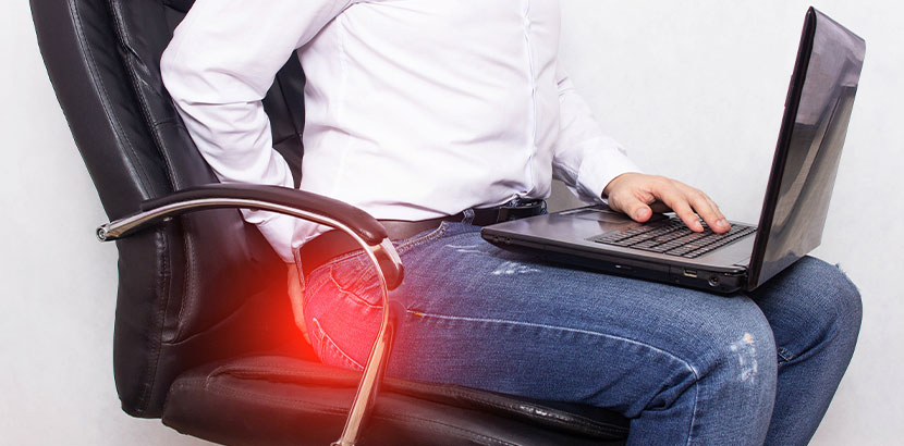 Ein Mann mit Laptop im Bürostuhl, der sich peinlich berührt nach seiner Hose fasst.