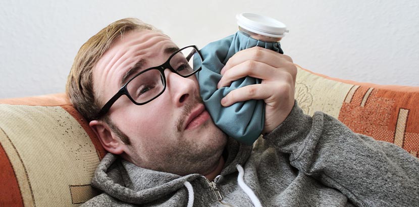 Ein Mann mit Schmerzen im Mund nutzt nach einem Eingriff einen Eisbeutel zur Betäubung.