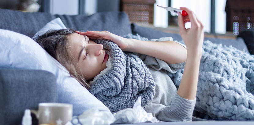 Eine Frau liegt mit grippalem Infekt auf dem Sofa und trinkt Kräuter Tee zum Schutz der Gesundheit.