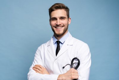 Ein Facharzt für Allgemeinmedizin vor blauem Hintergrund.