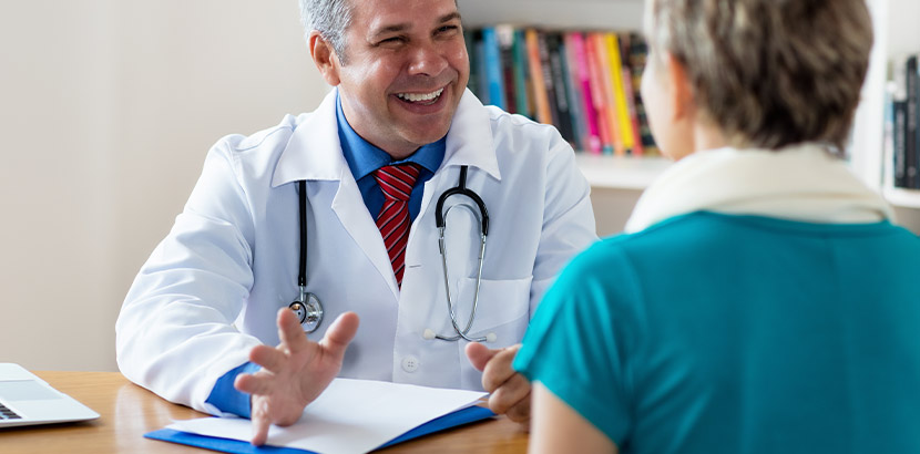 Ein Arzt für Allgemeinmedizin lächelt eine Patientin in der Sprechstunde an.