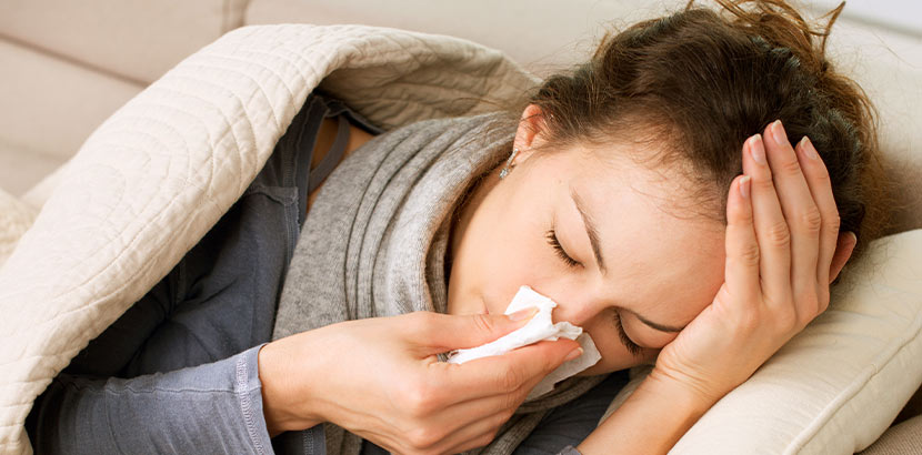 Eine Frau liegt mit Grippe auf dem Sofa.