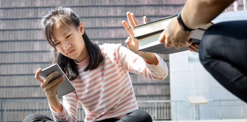 Mädchen mit Anzeichen für Aufmerksamkeitsdefizit-Syndrom schaut lieber auf ihr Smartphone-Handy als ein Buch zu lesen.