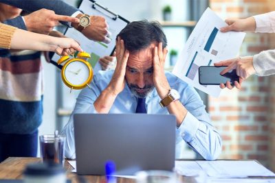 Geschäftsmann im Büro ist überfordert von zu vielen Tätigkeiten.