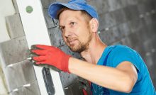 Handwerker bei Kontrolle und Verfugen von Wandfliesen auf Baustelle.