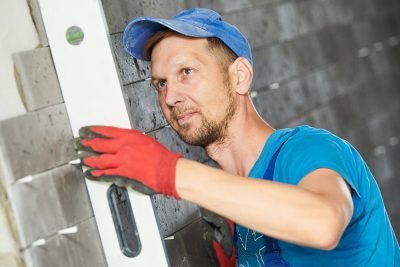 Handwerker bei Kontrolle und Verfugen von Wandfliesen auf Baustelle.