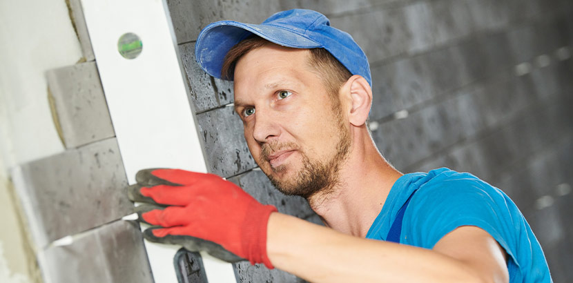 Handwerker bei Kontrolle und Verfugen von Wandfliesen auf Baustelle.