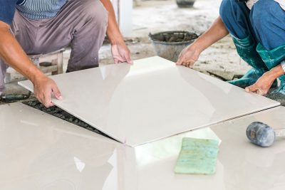 Zwei Meisterfliesenleger bei der Verfliesung mit einer Bodenplatte aus Keramik im Großformat.