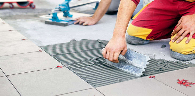 Handwerker verwendet Werkzeug beim Zuschneiden von Keramik-Fliesen und Auftragen von Fliesenkleber.