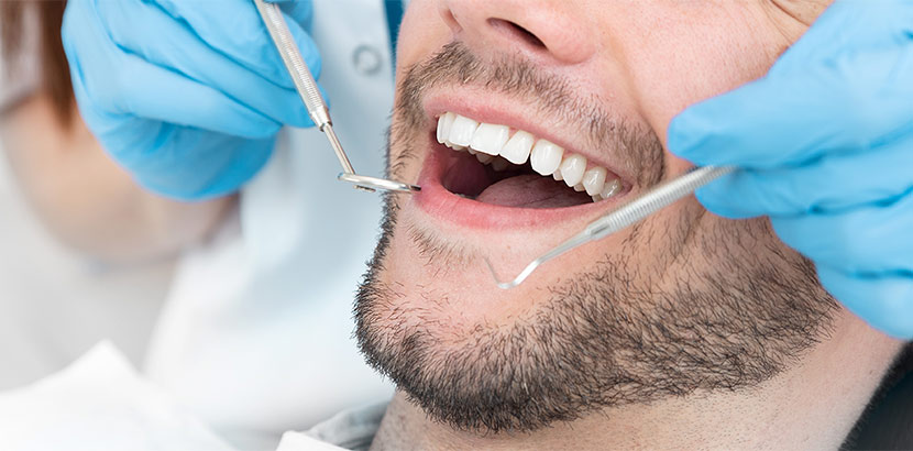 Arzt verwendet Sonde und Spiegel bei Zahnarzttermin in Arztpraxis für Kontrolle.