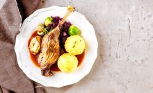 Teller befüllt mit Martinigansl in Sauce mit Knödel und Gemüse