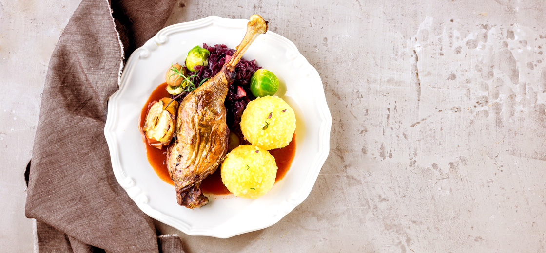 Teller befüllt mit Martinigansl in Sauce mit Knödel und Gemüse