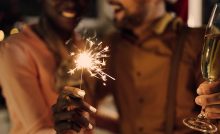 Ein junges Paar feiert mit Sekt und Wunderkerze Silvester zu Hause.