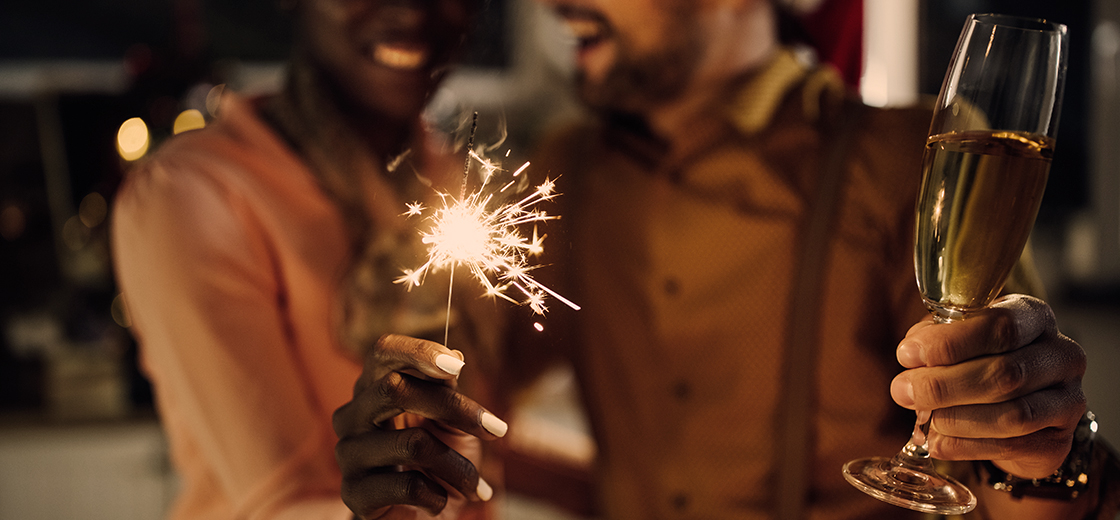 Ein junges Paar feiert mit Sekt und Wunderkerze Silvester zu Hause.