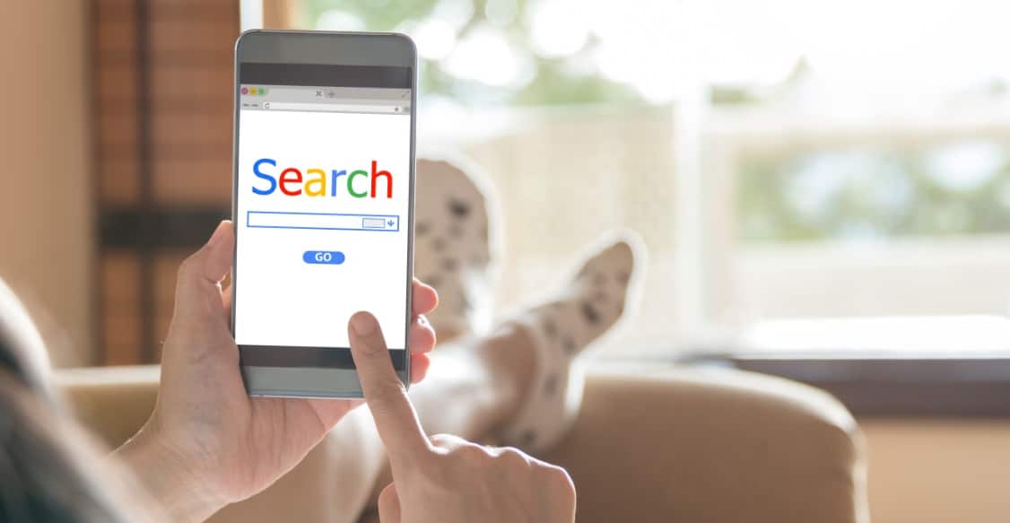Frau, die von daheim mit ihrem Smartphone über Google sucht und auf AdWords Anzeigen und Google Ads stößt.
