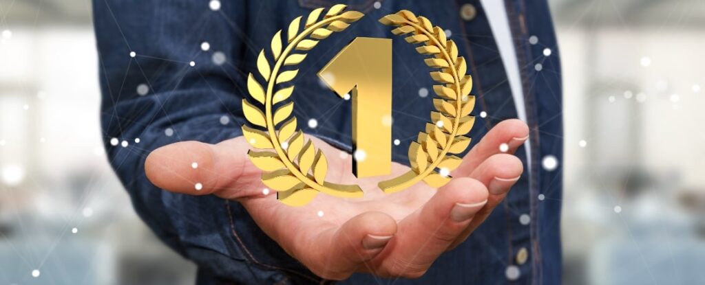 Geschäftsmann, der seine Hand ausstreckt, in der eine goldene eins mit Lorbeerkranz liegt. Den ersten Platz bei Google schafft nur, wer daran arbeitet, auf Google nach vorne zu kommen.