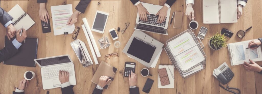 Holztisch, auf dem viele mobile Arbeitsgeräte liegen, an denen Leute gemeinsam arbeiten. Versinnbildlicht, wie ein CMS System funktioniert.