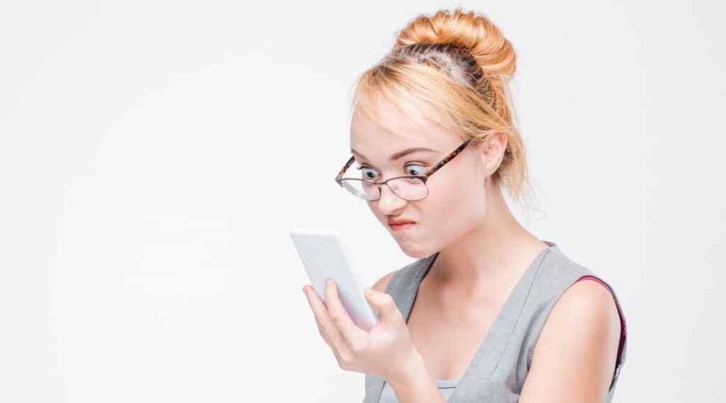 Junge blonde Frau mit Brille, die sich über eine Website ärgert, die nicht im Responsive Design erstellt wurde und daher am Handy schlecht lesbar ist.
