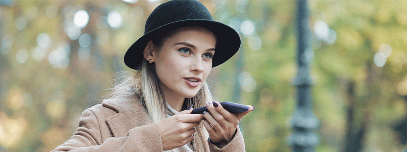 Junge blonde Frau, die via Voice Search eine Suchanfrage über ihr Smartphone aufgibt.