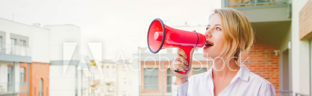 Junge blonde Frau. die mit einem Megafon auf ihrem Blakon steht und Werbung für ihre Website macht,
