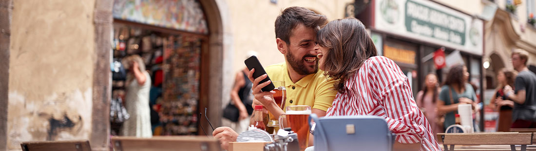 Junges glückliches Pärchen in einem Café, die mit dem Handy eine lokale Suche über Google absetzen.