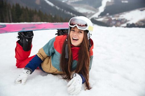 Junge Frau beim Wintersport, die lachend im Schnee liegt.